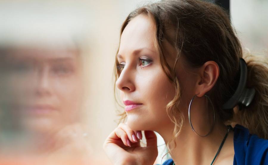 A young woman looking out a window represents how mental illness can disrupt your life.
