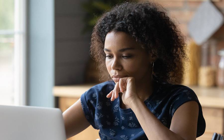 A young black woman looks at the computer while participating in a virtual support group for patients with stage IV breast cancer.