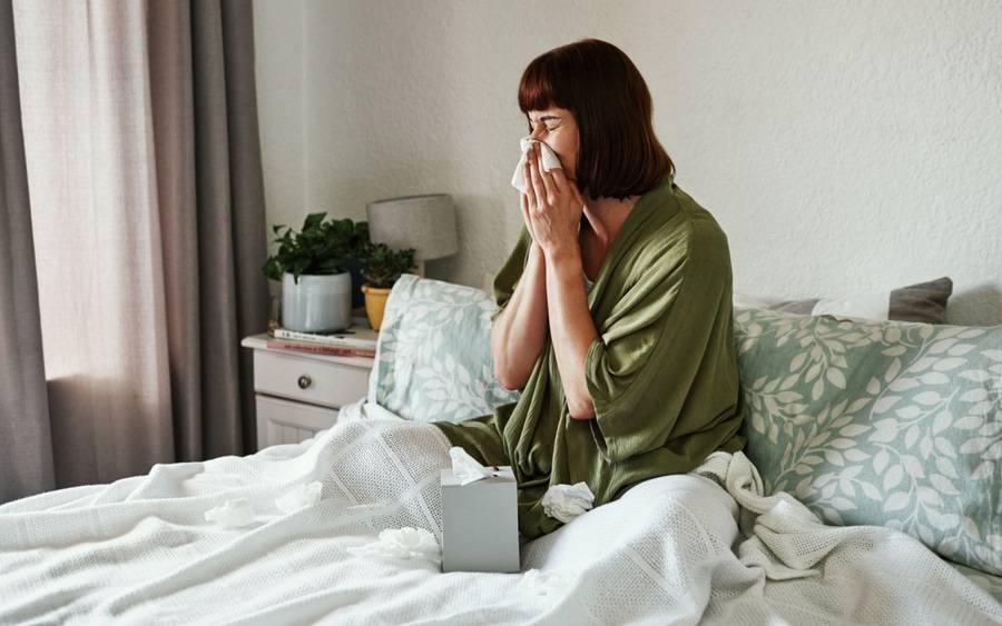 Woman in bed sneezing. Could it be a cold or the flu?