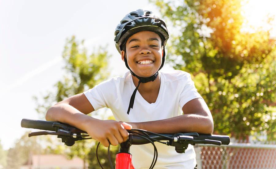 A young black male smiles as he sits on an ebike wearing a helmet for safety.