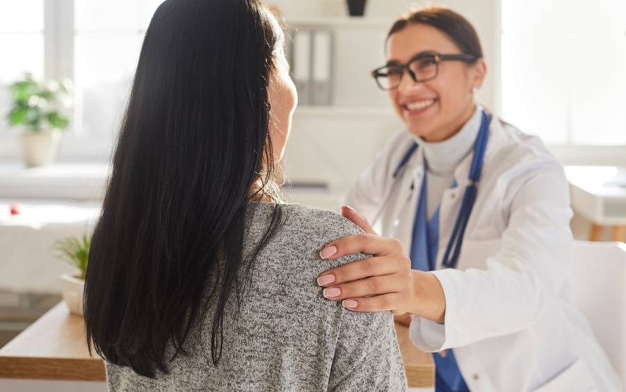 A friendly female doctor with glasses with a female patient discussing the patient's care.