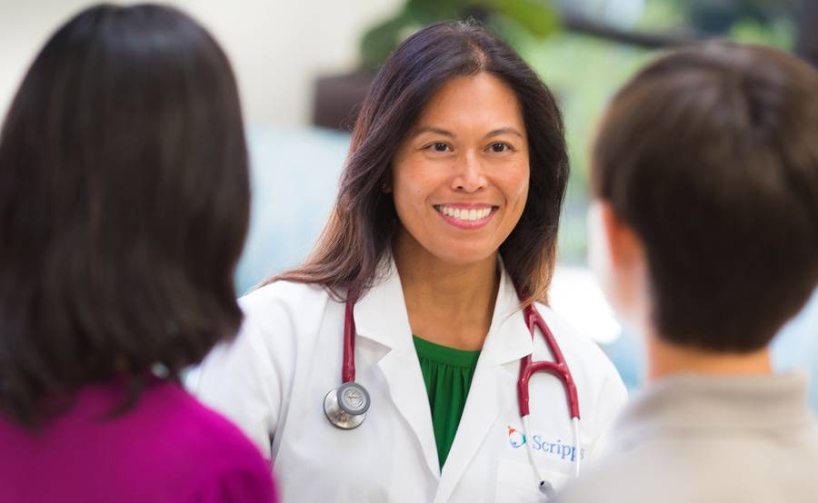 A female doctor smiles at two patients, representing why consumers should choose Scripps Health during open enrollment.