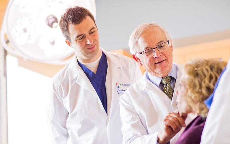 A mature male doctor guides a young male doctor in a skin examination, representing Scripps Clinic's skin cancer fellowship.