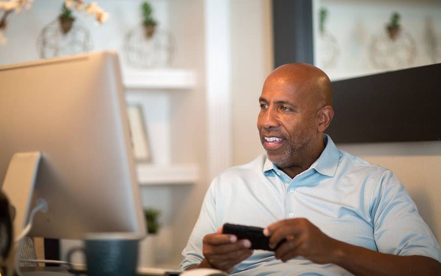 A middle aged man smiles as he participates in a men's support group for cancer from his home office.