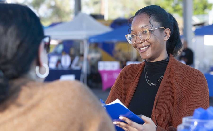 A multi-ethnic woman takes patient information at an outdoor health setting, representing health equity at Scripps.