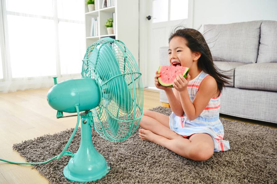 A little girl eats watermelon, has fan turned on to stay cool during hot weather.