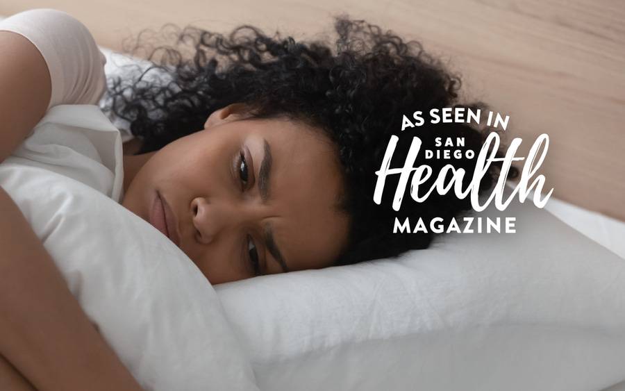 A young black woman lies in bed having trouble falling asleep.  San Diego Health Magazine