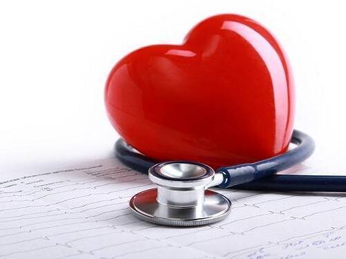 A stethoscope is wrapped around a red plastic heart on a heart scan printout.