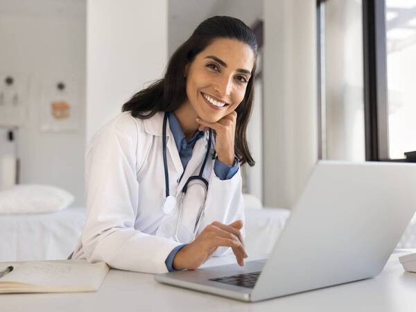 A woman doctor smiles while she sits at the computer representing a Scripps Health speaker series.