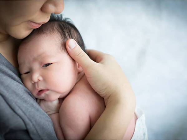 A woman nurtures a newborn in a diaper, holding them closely against her chest.