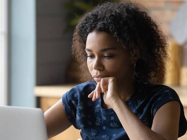 A young black woman looks at the computer while participating in a virtual support group for patients with stage IV cancer.