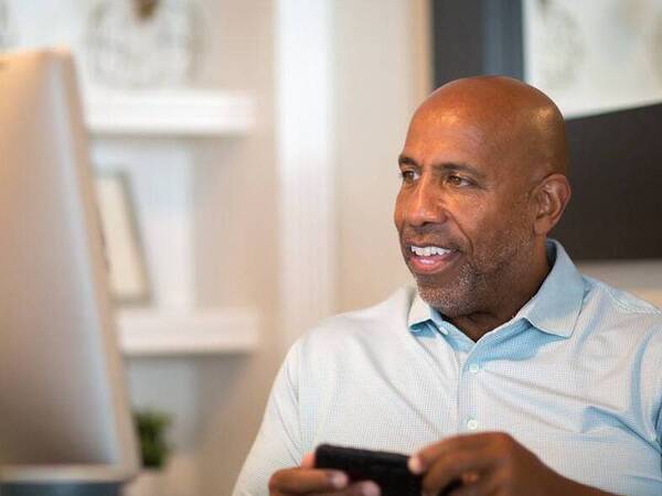 A middle aged man smiles as he participates in a men's support group for cancer from his home office.