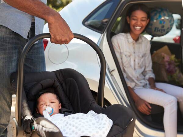 A young couple get ready to buckle their new baby into the backseat of their car.