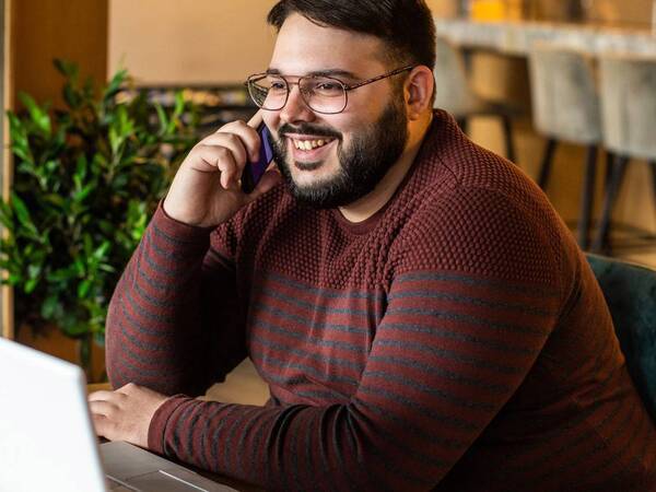 A young man talks on a mobile phone in front of a laptop computer.