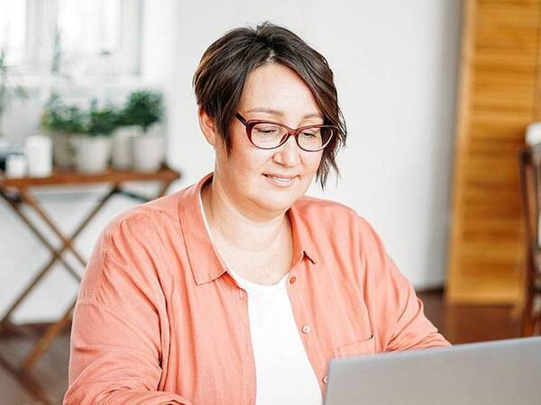 A woman in a home office looks at her laptop.