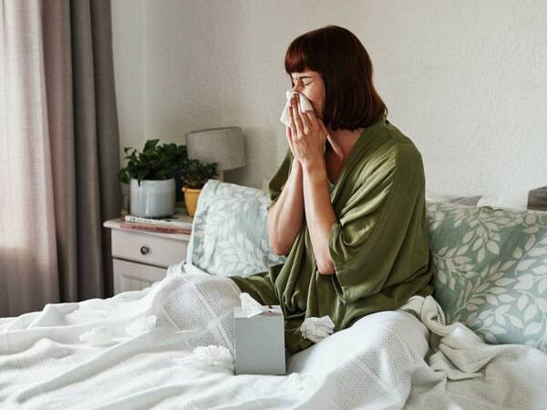 Woman in bed sneezing. Could it be a cold or the flu?