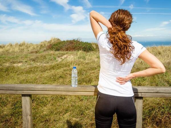 A woman wearing athletic apparel stretches to help relieve back pain.