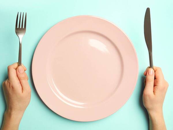 A person holds a fork and knife next to an empty, representing grouchy and short-tempered feelings at mealtimes.