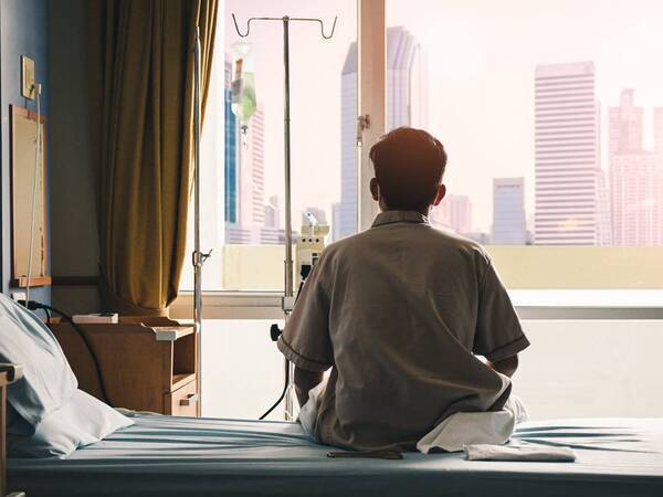 A hospital patient sits on a hospital bed looking out the window as he waits to be discharged.