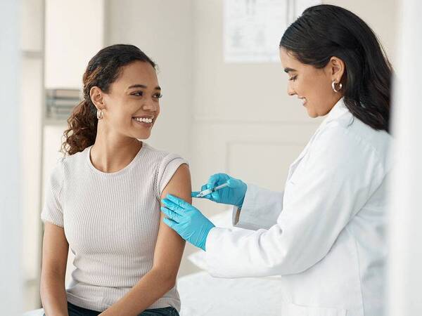 A young woman in a grey shirt receiving a vaccine from a provider illustrates the Flu Season vaccinatio