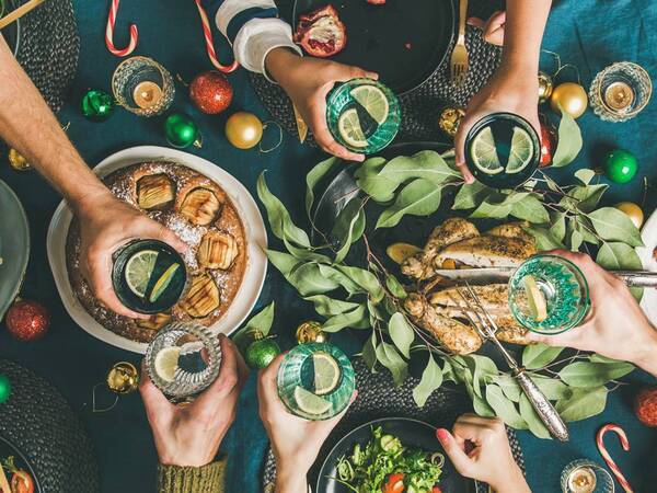 People lift their glasses to celebrate a festive holiday meal with healthy food displayed including pomegranates, turkey, salad and butternut squash.