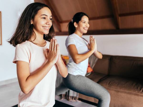 Two young women smile as they practice yoga on a mat indoors.