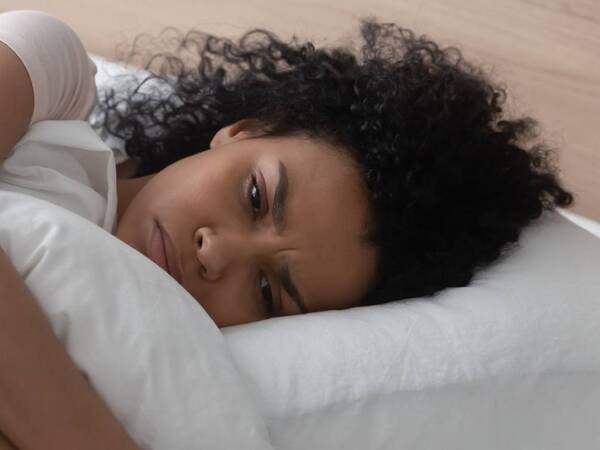 A young black woman lies in bed having trouble falling asleep. 