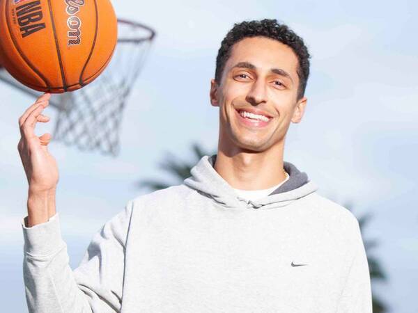 Bahrom Firozgary, MD, sports medicine physician at Scripps Clinic Torrey Pines, smiles on the basketball court as he balances a basketball on his finger.