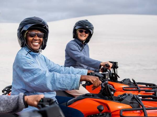 Two adults smile as they get ready to ride an ATV each wearing a helmet with a desert landscape in the background.