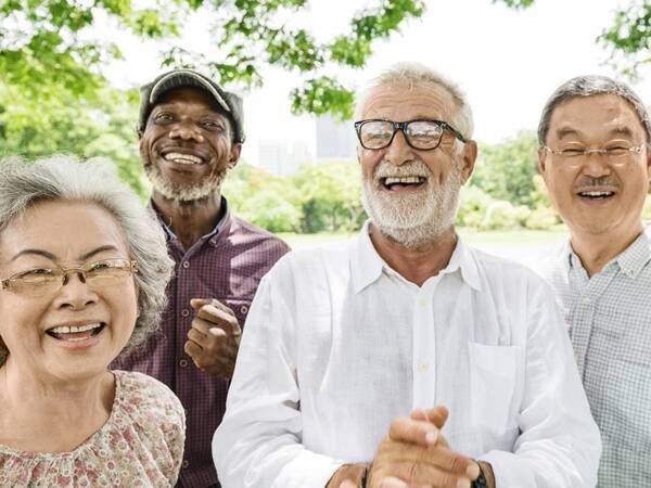 A group of diverse senior adults smile and laugh in an outdoor setting. 