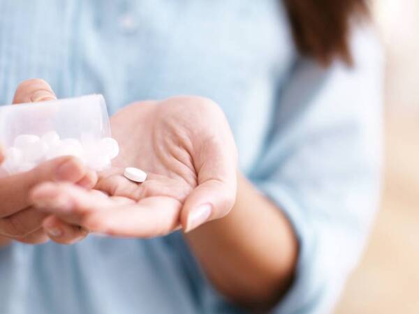 A woman tips a pill bottle dropping a couple of aspirin in her hand.