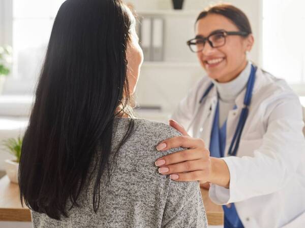 A friendly female doctor with glasses with a female patient discussing the patient's care.