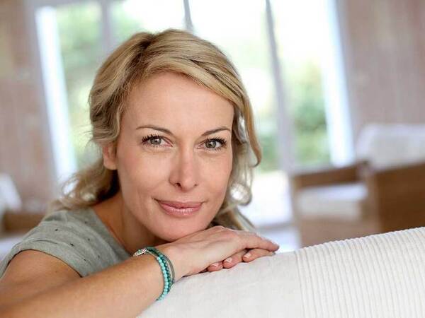 Smiling middle-aged woman looking over the back of a couch.