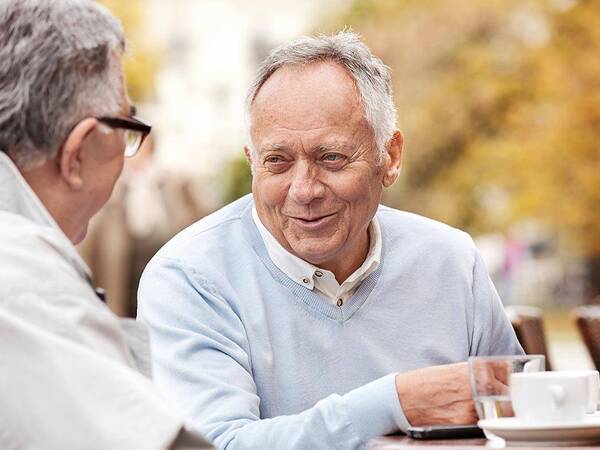 A smiling mature man having coffee with a friend represents the importance of lung cancer screening and prevention.
