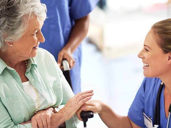 A smiling female nurse kneels down to greet a mature Caucasian woman in a wheelchair, representing how Scripps keeps you informed at every step  of your cancer journey.