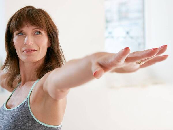 A middle-aged woman practices a yoga pose in a sports bra, representing the confidence gained from breast augmentation.