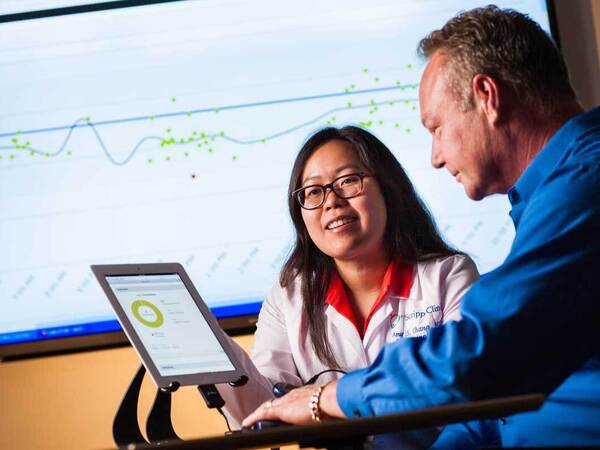 A Scripps diabetes clinical professional works closely with a patient diagnosed with diabetes in a seated desk setting with a large screen in the background. 