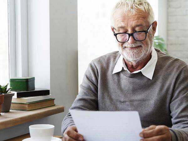 A smiling mature man reads paperwork over a cup of coffee, representing the improved quality of life that can be gained from quick treatment for stroke.