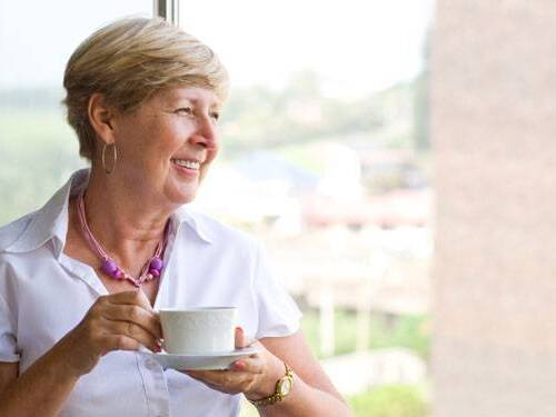 Smiling mature woman looks out the window with a cup of tea.